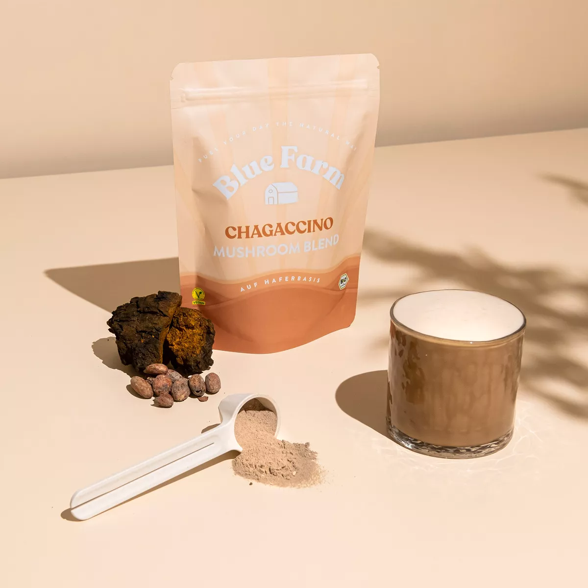 Ein Pulver mit Chagaccino steht auf einem Tisch, davor ein Glas mit angerührtem Chagaccino als Kaffee-Alternative.