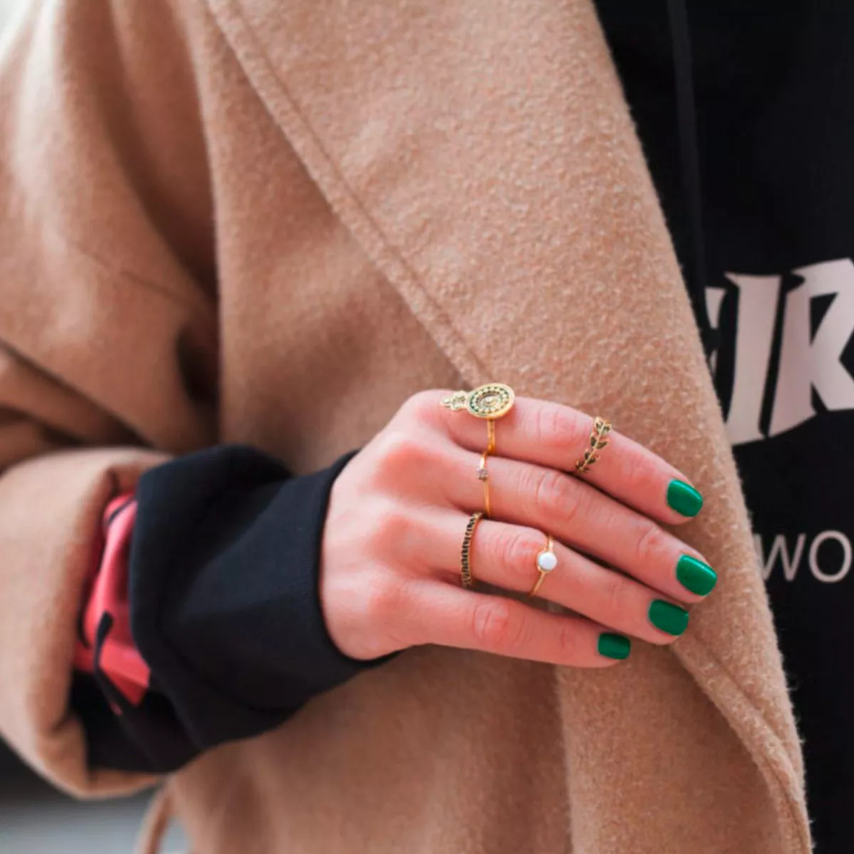 Modestil: Eine Frau mit brauner Jacke, schwarzem Pullover und grünen Nägeln.