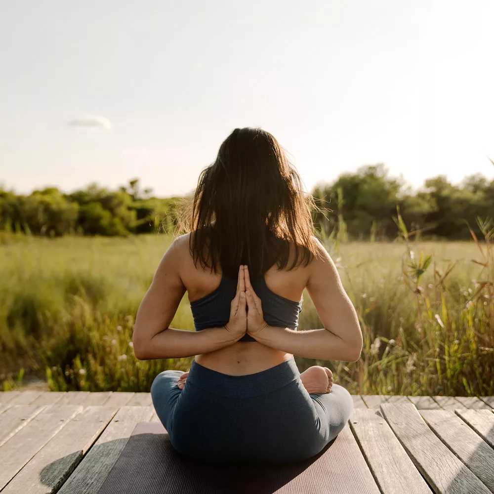 Yin Yoga: Frau sitzt im Schneidersitz und hat ihre Hände hinter dem Rücken gefaltet