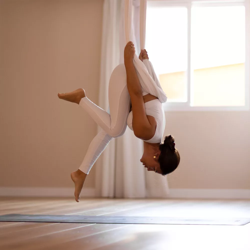 Eine Frau macht Aerial Yoga über Kopf.