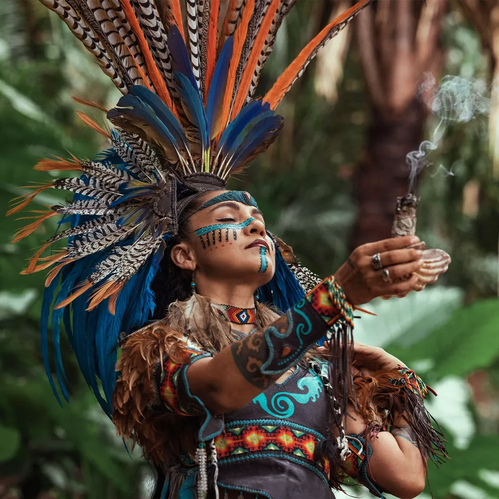 Eine Maya-Frau hält ein Räucherbündel in die Luft.