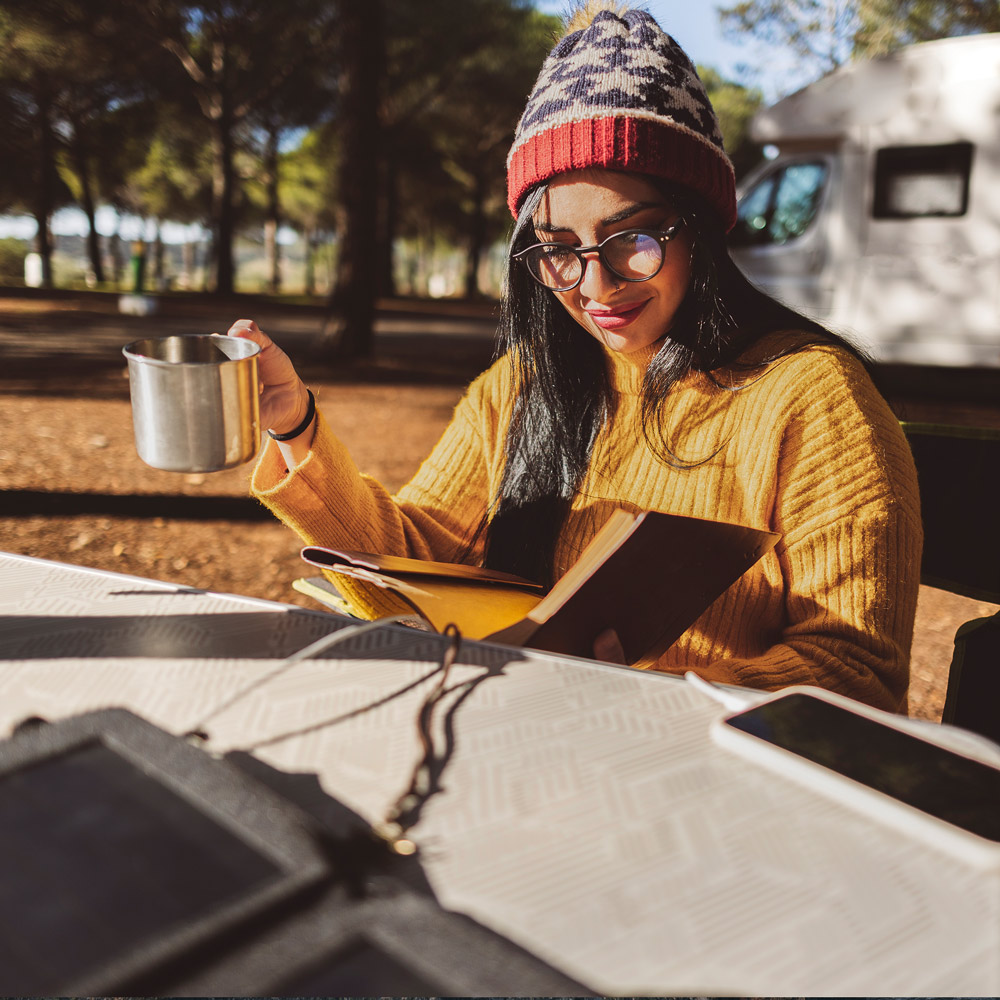 Solar Camping: Frau lädt ihr Handy über mobile Solarmodule, während sie liest