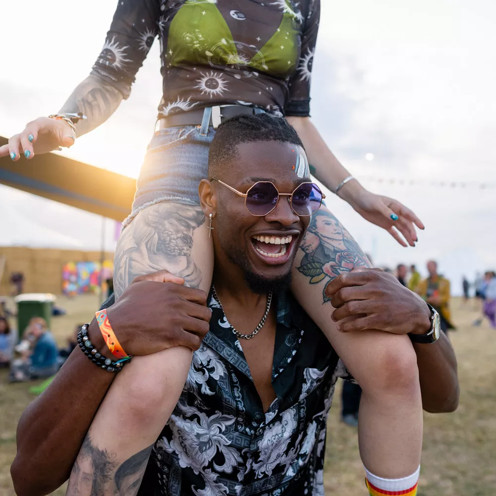 Sonnenschutz auf dem Festival: Mann mit Sonnenbrille, der eine Frau auf den Schultern trägt