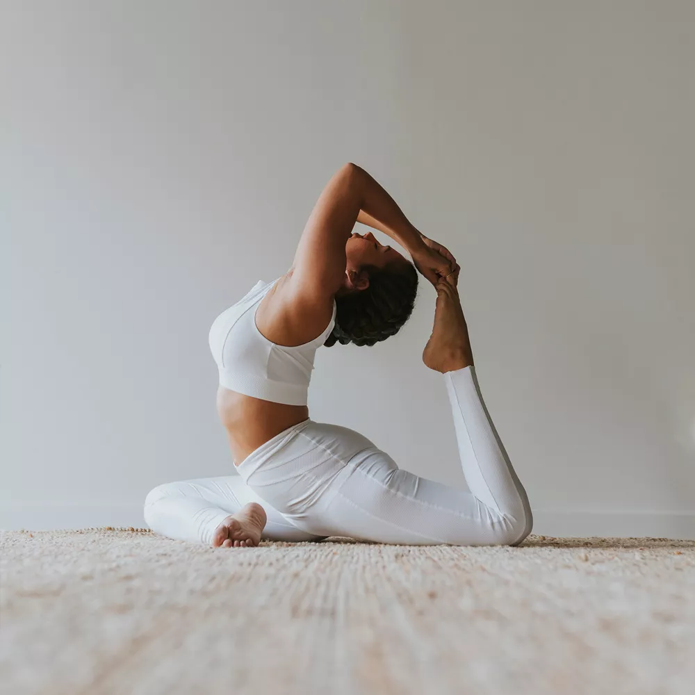 Eine Frau praktiziert Yoga vor einer weißen Wand.
