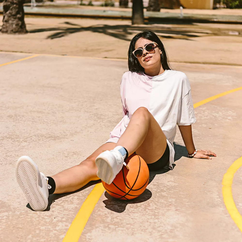 Eine Frau sitz auf einem Basketballplatz und trägt Sonnebrille.