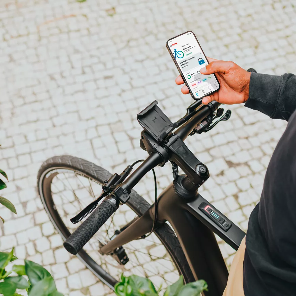 Mann der auf E-Bike sitzt, hält Smartphone in der Hand. Auf dem Display ist die eBike Flow App zu sehen