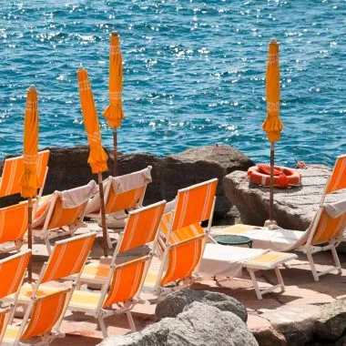 Italienische Insel: orangene Sonnenschirme auf einer Steinbucht.