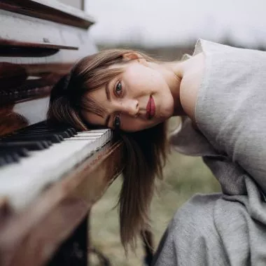 Die Wirkung von Musik auf das Gehirn: Frau legt ihren Kopf auf die Tasten des Klaviers und lächelt