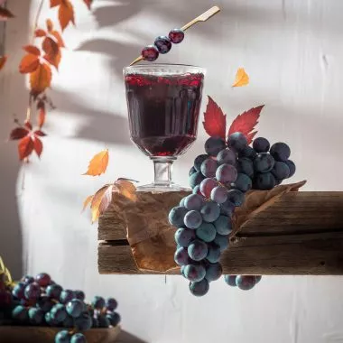 Ein Weinglas steht mitsamt ein paar Trauben auf einem Holzbalken.