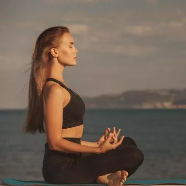 Vinyasa Yoga: Frau meditiert am See