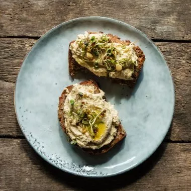 Zwei Brote mit Auberginen Hummus und Sprouts belegt auf einem Teller.