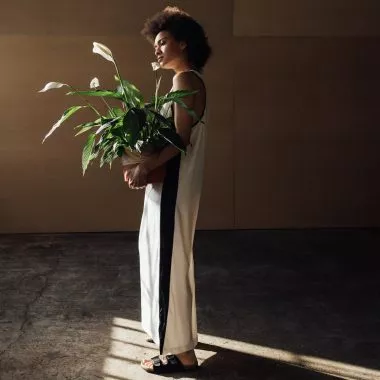 Eine Frau steht in einem halbdunklen Raum und hält eine Pflanze in der Hand.